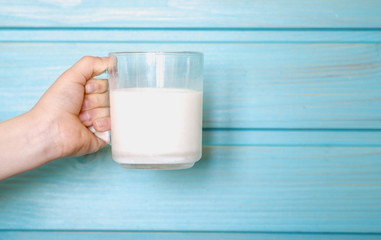 Hand of a child with a glass of fresh milk against a blue wooden wall