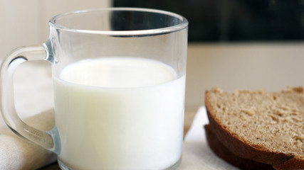 A glass of milk next to a slice of rye bread on the table
