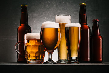 close up view of bottles and mugs of beer on grey background