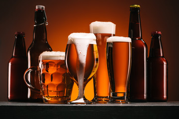 close up view of bottles and mugs of beer on orange background