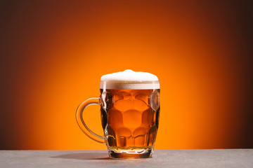 close up view of mug of cold beer on orange backdrop