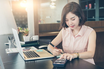 Beautiful business woman working on desk with calculator and  writing on paper.