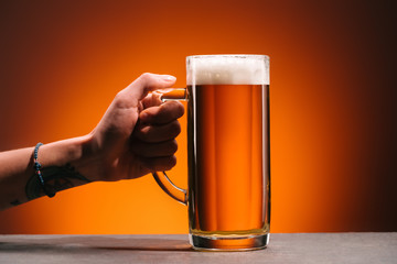 cropped shot of woman holding glass of cold beer with foam on orange backdrop