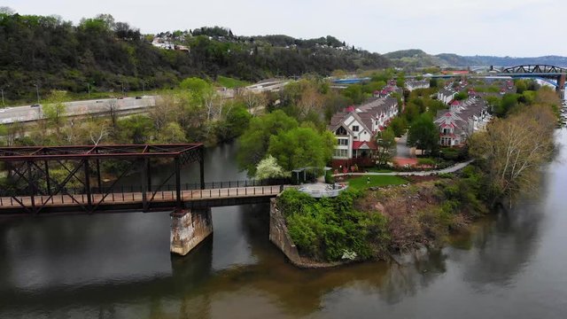 A daytime forward aerial establishing shot of Harrs Island in Pittsburgh as a bicyclist rides across the pedestrian bridge.  	