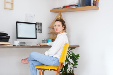 Portrait of attractive serious confident female architect sits at work place,reads information on web page, surfes internet, looking at camera in office. People, business, modern technology concept.