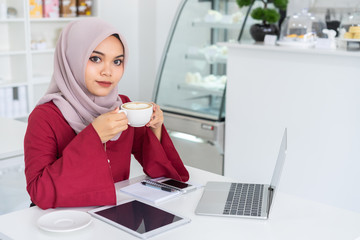 Asian muslim business woman working with laptop and black screen tablet for graphic montage.