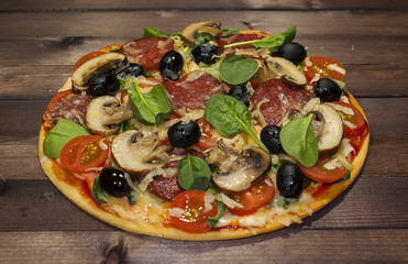 Traditional hot Italian pizza on a thin dough with salami, mushrooms, olives on a wooden table. Only taken out of the oven.