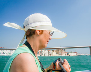 Fototapeta premium Mature tourist woman travelling in Italy sails on boat in Venice and shoots video.