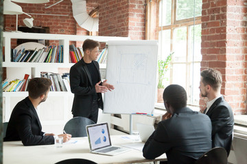 Business briefing in multiethnic work group with ambitious male explaining financial graph to thinking coworkers. Visual ideas on flipchart. Concept of diversity, brainstorming, cooperation