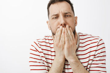 Guy drink lots of alcohol, feeling hangover and stomach disorder. Portrait of sick funny guy in casual clothes, covering mouth with palms, feeling dizzy and wanting vomit or puke over gray wall - obrazy, fototapety, plakaty