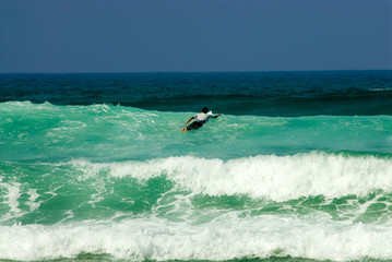 Surfer at the top of turquoise wave swimming towards deep dark sea