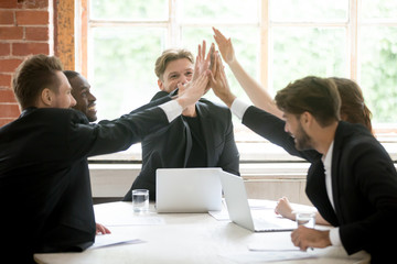 Multiracial work team giving high five happy after successful business deal at briefing. Managers satisfied with company income, rates growth on stock exchange. Concept of strength, good motivation