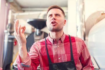 Portrait of happy barista in apron on background of industrial coffee grinder