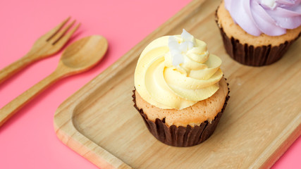 Cupcake on a wooden plate and pink background.