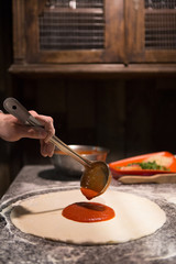 Chef hand spreading tomato paste on pizza base