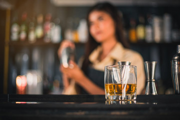 Bartender is adding ingredient in shaker at counter. Bartender is mixing alcohol in a shaker to serve customers.