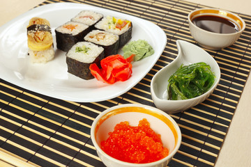 Sushi and rolls with ginger and wasabi, hiyashi wakame salad, soy sauce and salmon caviar on a black bamboo mat close up.