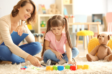 Female psychologist with cute little girl during play therapy