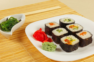 Assorted sushi, hiyashi wakame salad with ginger and wasabi on a bamboo mat close up.