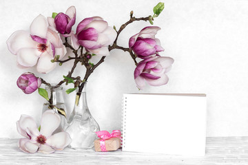 Creative layout made with pink magnolia flowers, empty card and gift box on white wooden background