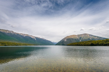 Lake Rotoiti, Tasman, Nelson Lakes, New Zealand: Beautiful scenic view to great mountain range lake with wooden jetty pier and pretty smooth reflections on the water surface at a cloudy rainy day