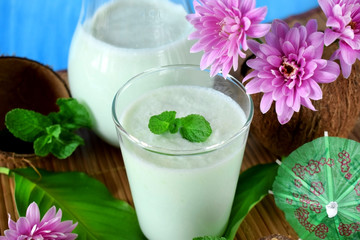 Coconut milkshake with mint flavour in a glass surrounded by coconut shells and pink flowers