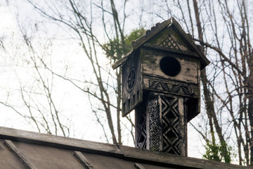 An old carved bird house on the roof of the house. The birdhouse.