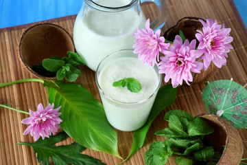 Coconut milkshake with mint flavour in a glass surrounded by coconut shells and pink flowers
