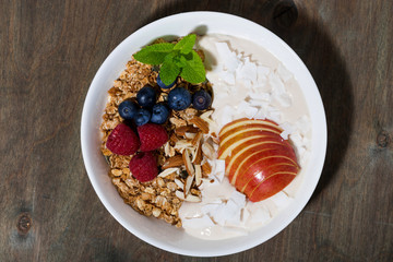 oat granola with apples and berries on wooden background, top view