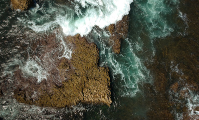 Aerial view of sea waves crash on the rocks in the coastline