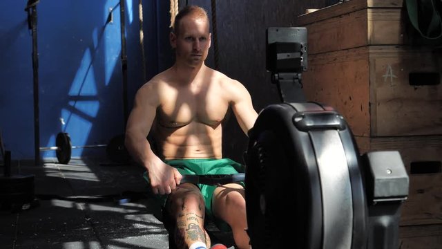 Muscular young shirtless man, training back on equipment, pulling cable at rowing machine. Tattoo says Don't stop dreaming, there's still time
