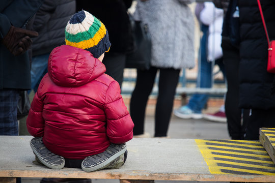 Niño sentado entre la gente en un dia de frio