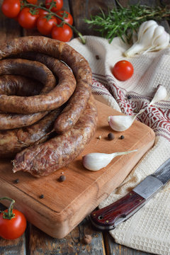 Traditional smoked sausage ring in a rustic style. Appetizing sausages made of pork and lamb with fresh herbs, spices on the wooden board. Free space for text.