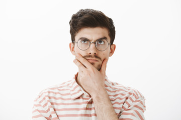 Portrait of determined focused and creative male with funny moustache, rubbing chin, looking up while thinking, making up idea or concept, trying to solve hard mathematic problem, making calculations