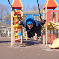 Cheerful European boy swinging at a playground.