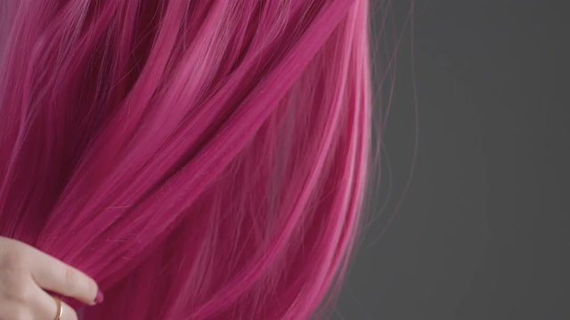 Closeup of pink hair creative colored texture. Woman's hand take off hair and let us see grey background