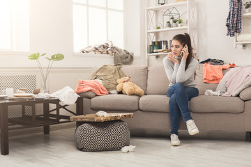 Desperate woman sitting on sofa in messy room