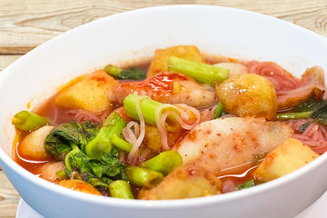 Thai food.Pink seafood flat noodles.Spicy lemongrass flavored soup with pork, chicken on wood background.Close up.Clipping path