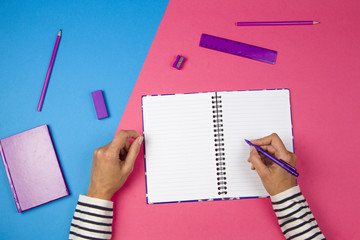 Woman hands writing to open notebook and office supplies on colorful background