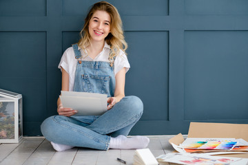 creative leisure. painting hobby. smiling young beautiful female artist sitting at home holding at her artwork