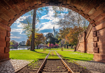 Tunnel view of Frankfurt, Germany in spring. Park with green grass, trees and blue sky. Skyscrapers in the background.