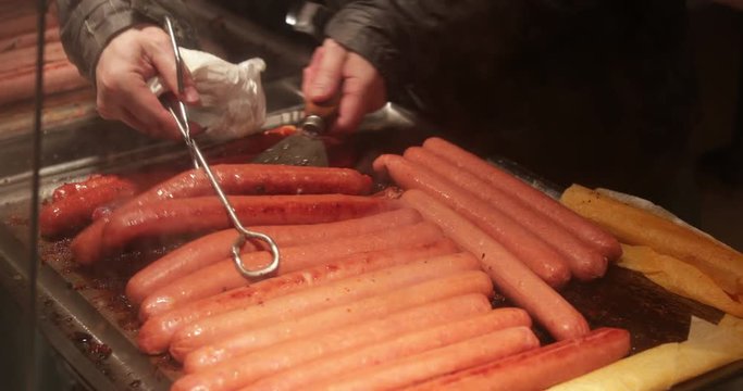 Sausages on plate grill in 4K. Picking up multiple hot dogs on plate grill