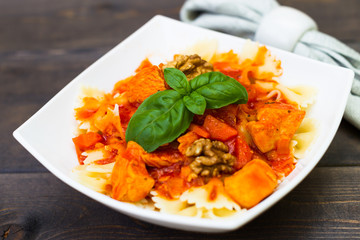 Italian pasta - butterfly macaroni (bows) of Farfarello with tomato sauce on a white plate and on a dark wooden background.