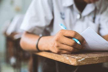 Close up to students writing and reading exam answer sheets exercises in classroom of school with...