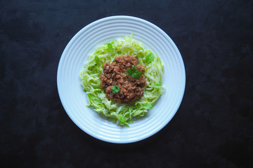 Plate of zucchini spaghetti with beef bolognese on black background.