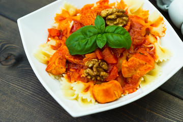 Italian pasta - butterfly macaroni (bows) of Farfarello with tomato sauce on a white plate and on a dark wooden background.