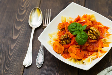 Italian pasta - butterfly macaroni (bows) of Farfarello with tomato sauce on a white plate and on a dark wooden background.