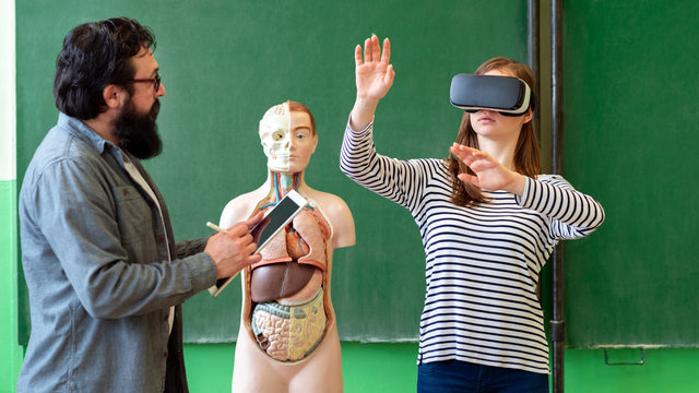 Young Teacher Using Virtual Reality Glasses And 3D Presentation To Teach Students In Biology Class. Education, VR, Tutoring, New Technologies And Teaching Methods Concept.