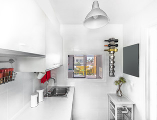 Modern interior decoration of a bright kitchen with white counter and cabinets, washing machine, microwave, sink, tray and accesories in red