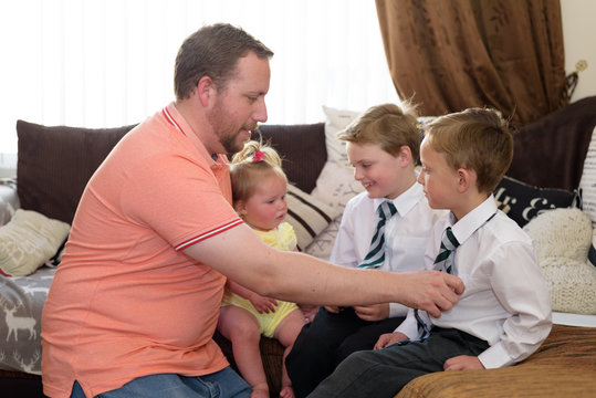 Father getting two sons dressed for school at home whilst holding baby girl in arms